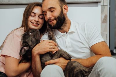 Happy man and cheerful young woman hugging with their lovely pet, small french bulldog with family