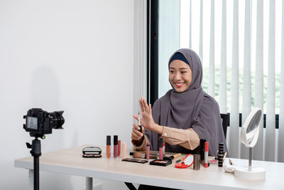 Young woman blogging while applying make up at office