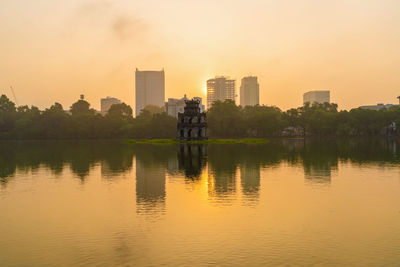 Scenic view of lake by buildings against sky during sunset