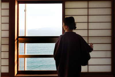 Rear view of woman looking at sea through window