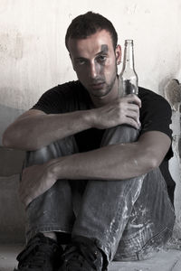 Portrait of young man sitting against wall