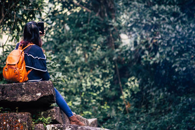 Side view of woman sitting on land in forest