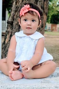 Baby girl smiling while sitting on marble by tree