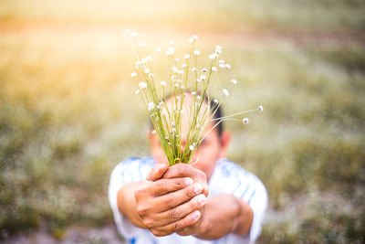 Close-up of man holding flowers on field