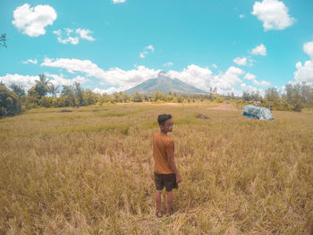 Portrait of young man standing on grassy field against sky