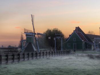 Traditional windmill on field against sky during sunset