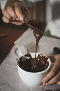 Cropped image of person dipping chocolate in container at home