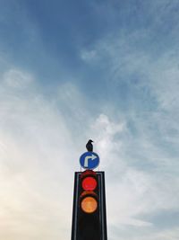 Low angle view of bird perching traffic signal against sky during sunset