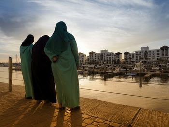 Rear view of women wearing burka while standing by river against sky