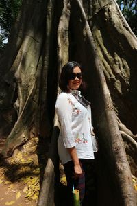 Woman standing by tree trunk in forest