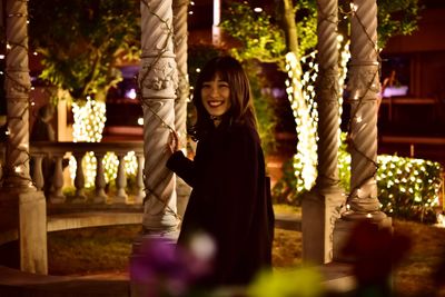 Portrait of smiling woman standing by column at night
