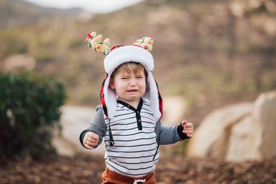 Toddler wearing deer horns christmas hat and crying.