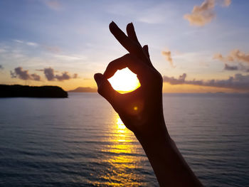 Cropped hand showing ok sign at beach during sunset