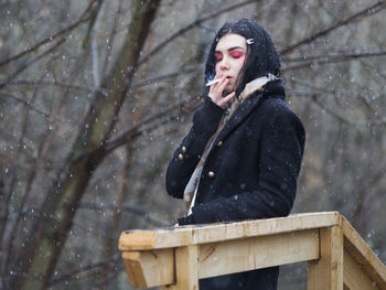 Young woman smoking cigarette while standing in snow