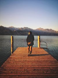 Rear view of man on pier over lake against sky