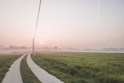 Road amidst field against sky during foggy weather