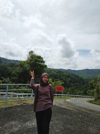 Woman gesturing peace sign against cloudy sky