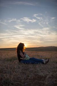 Full length of woman with baby sitting on field during sunset