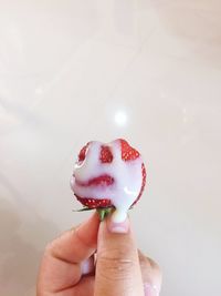 Cropped hand holding strawberry with cream over tiled floor