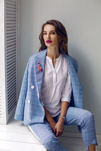 Business woman in a blue suit sits at the big window in the white room