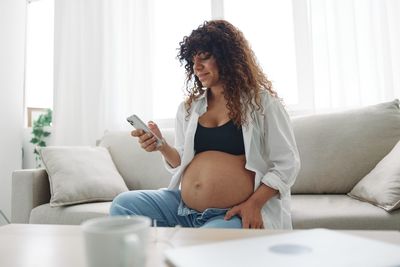 Young woman using phone while sitting on sofa at home