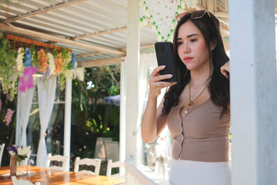 Young woman holding smart phone while sanding outdoors
