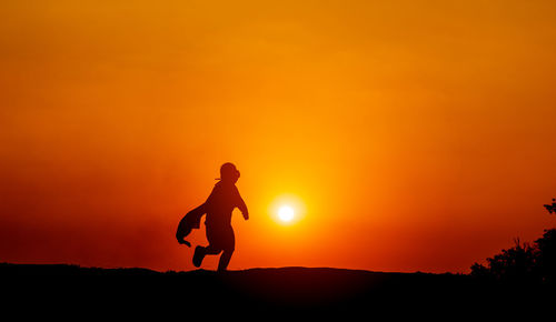 Silhouette man standing against orange sky during sunset