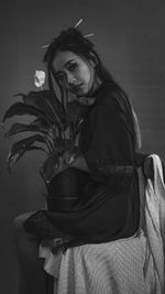 Portrait of young woman holding plant while sitting on chair against wall