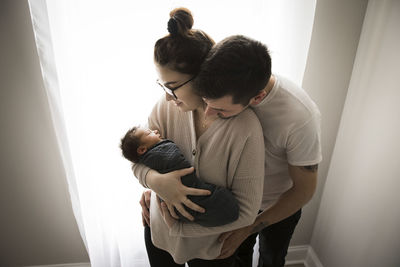 Gen z parents snuggle by window and admire their newborn baby