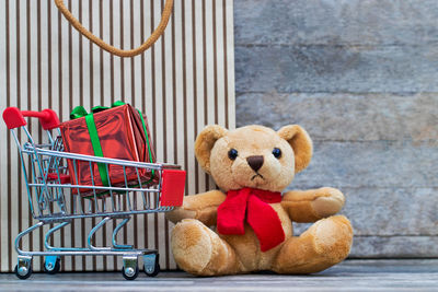 Close-up of stuffed toy by gift box in shopping cart against wall