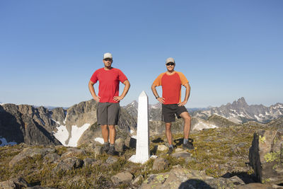 Two trail runners stand at the border marker, canada / united state