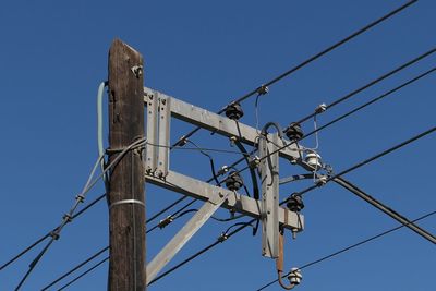 Low angle view of electricity pylon against blue sky