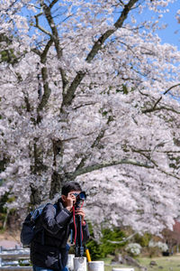 Man photographing while standing against cherry tree