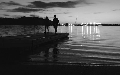 Silhouette couple walking on jetty at sea during dusk