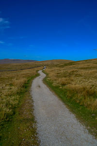 Empty road amidst field against blue sky