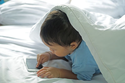 High angle view of baby boy using phone while lying on bed at home