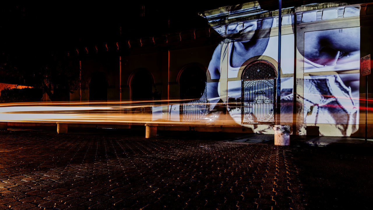 LIGHT TRAILS ON STREET AGAINST ILLUMINATED BUILDINGS AT NIGHT