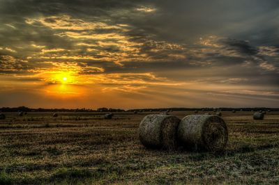 Hay bales on field against sky during sunset