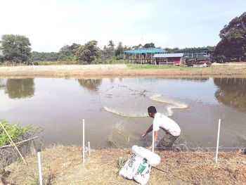 Rear view of man sitting by lake against sky