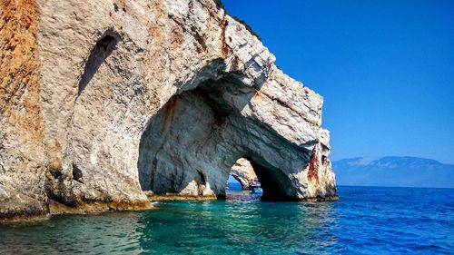 Rock formations in sea against clear blue sky