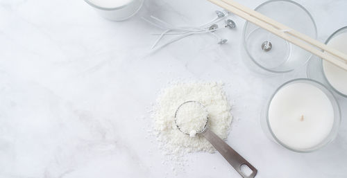 Ingredients for candle making , soy wax flakes, candles, wicks on light marble background