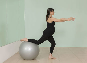 Full length of woman with arms raised against wall