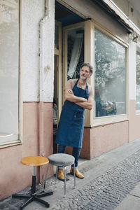 Full length of male upholstery worker standing with arms crossed at entrance of workshop