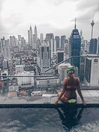 Full length of man and woman in swimming pool against buildings in city