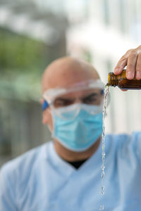 Doctor wearing protective mask and medical safety goggles holding a bottle pouring medical syrup