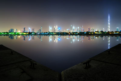 Illuminated city by sea against sky at night