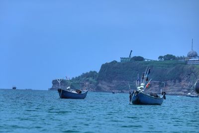 Boats sailing in sea against clear blue sky