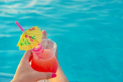 Cropped image of hand holding drink against swimming pool