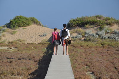 Rear view of friends walking on boardwalk against clear sky