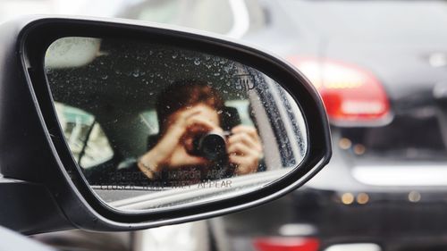 Reflection of man photographing in car side-view mirror